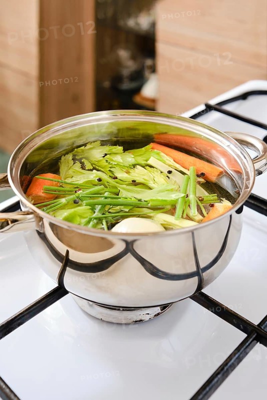 Fresh vegetables are being cooked in a pot on a stove. Cooking vegetable broth