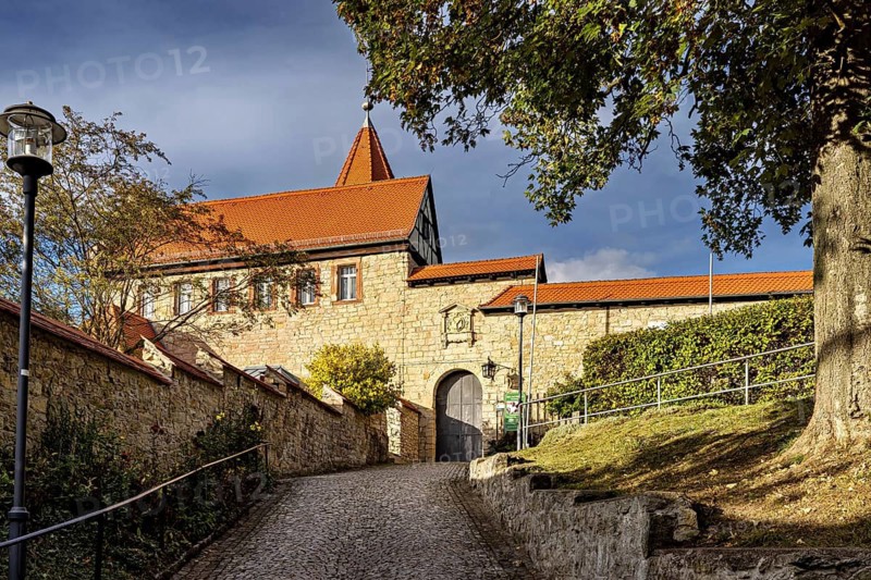Old building with red roof and massive brick walls along a paved path, The Lower Castle of Kranichfeld in Thuringia