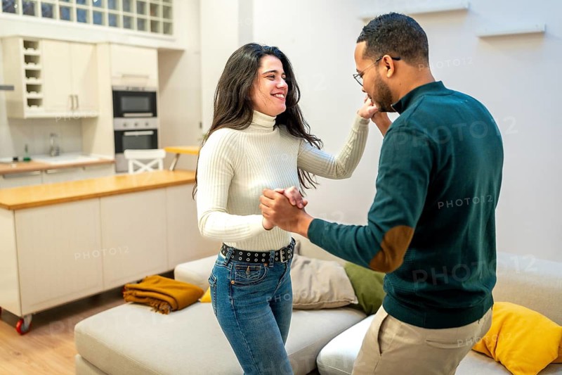 Happy young couple laughing and enjoying a romantic dance together in their modern apartment, celebrating love and togetherness in a relaxed home setting