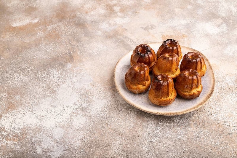 Golden caramelized Canele cookies dessert, cup of coffee, on brown concrete background, copy space, side view