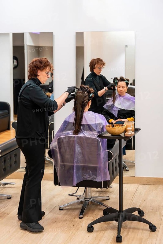 Hairdresser wearing gloves applying hair dye to a female client's long hair in sections, preparing for a color change service during a professional beauty appointment at the salon