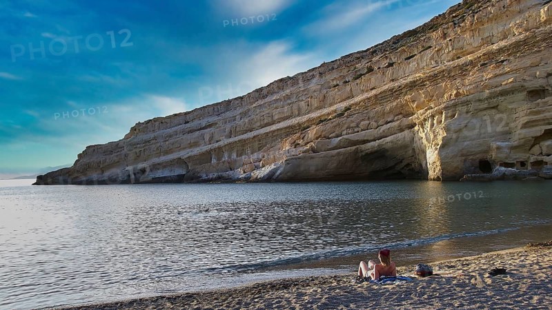Neolithic caves, former hippie paradise, rocky coast with calm sea and blue sky, two people on the beach, Matala, south coast, Crete, Greek Islands, Greece