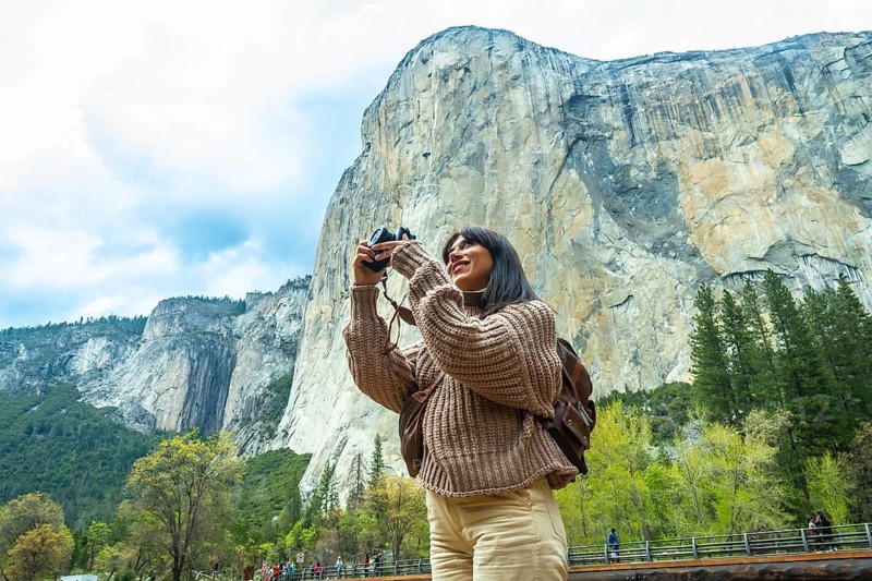 Woman traveler enjoying the natural beauty of yosemite national park, capturing the iconic el capitan granite monolith with her camera on a bright outdoor adventure day