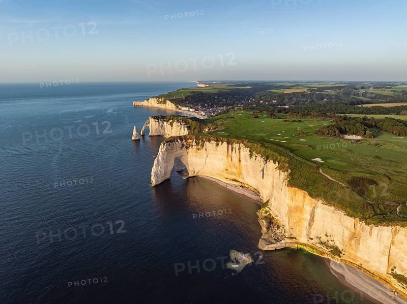 Aerial view of the rock gate La Manneporte in the evening sun, behind it the Porte d'Aval rock formation, well-known sights on the chalk coast with the distinctive rock pin, behind it the holiday resort of Étretat with the beach, on the horizon the Falaise d'Amont cliffs, right on the cliffs of the Golf d'Étretat golf course founded in 1908, Alabaster Coast, La Côte d'Albâtre, chalk cliffs, English Channel, Seine-Maritime, Normandy, France