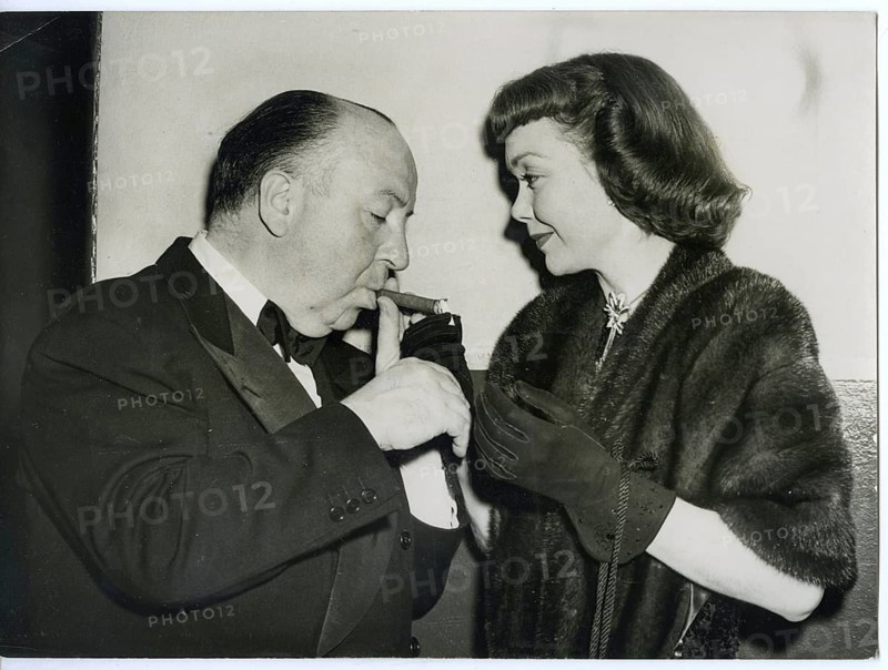 Alfred Hitchcock, Jane Wyman, actress, Hollywood, cigar, elegance, fur coat, elegant couple in formal dress interacting with cigars in an intimate moment, 1949, USA