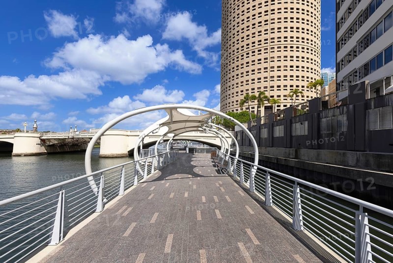 Wide view of the modern Tampa Riverwalk with a distinctive Rivergate Tower and a bridge over the Hillsborough River in Florida