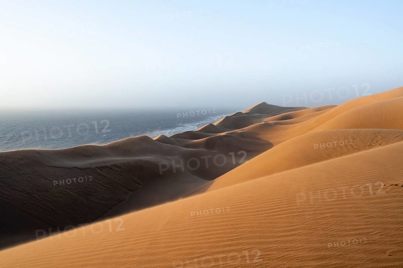 Sand dunes and sea in evening light, impressive desert landscape at sunset, sandy desert, Sandwich Harbour, Namib Naukluft Park, Namib Desert, Namibia