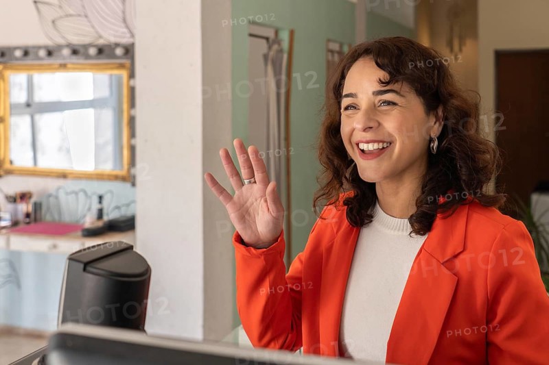 Smiling beauty salon owner waving a greeting while standing at the reception desk of a modern beauty salon