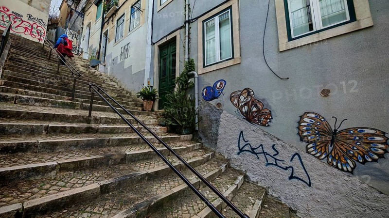 Butterfly graffiti on a wall next to a steep paved stone staircase, a person running up, Lisbon, Portugal
