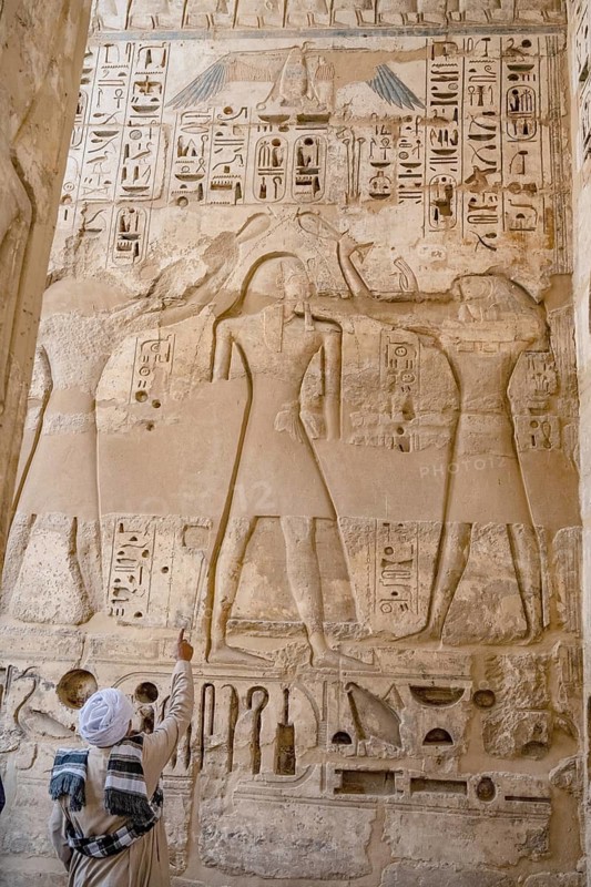 A tour guide points out details of reliefs and hieroglyphs inside Medinat Habu, the ancient Egyptian Mortuary Temple of Ramesses III on the West Bank of The Nile, Luxor, Egypt