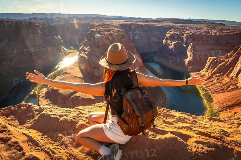 Woman feeling freedom while sitting overlooking the iconic horseshoe bend, a meander of the colorado river, during a sunny day trip, experiencing travel and adventure in the arizona desert landscape