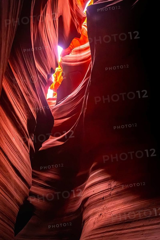 Antelope canyon slot canyon showing narrow sandstone formations with swirling lines and rich orange, red, and purple colors from sunlight filtering through the opening above
