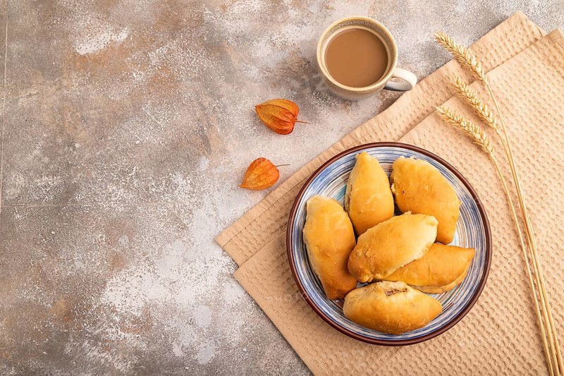 Homemade pies with jam and curd, cup of coffee, on brown concrete background with beige textile, copy space, top view, flat lay