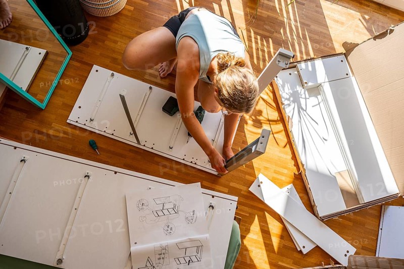 Young woman setting up a shelf, furniture assembly with screwdriver, IKEA furniture in a new apartment, moving