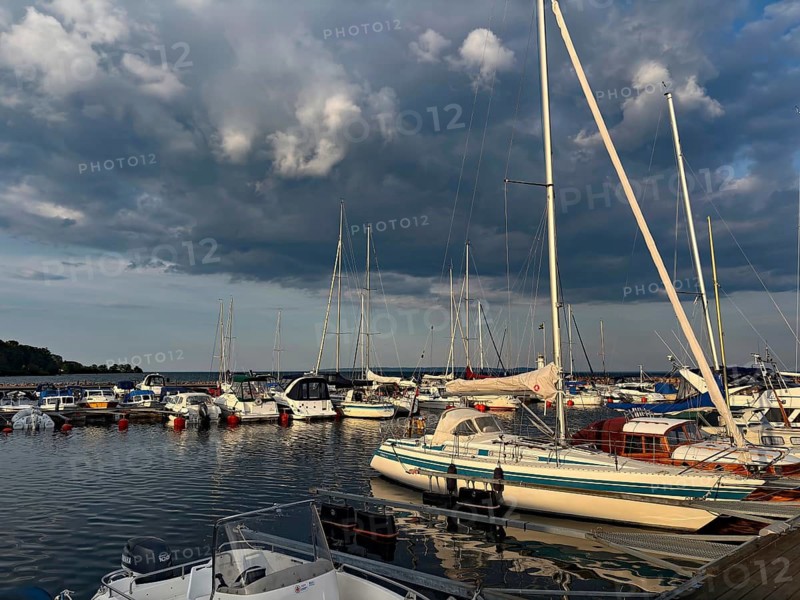 Yachts in harbor under dramatic cloudy skies, calm water and soft evening light create a peaceful atmosphere, Hjo, Lake Vättern, Sweden