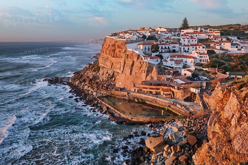 Stunning seaside village of Azenhas do Mar in Portugal as the sun sets over the Atlantic Ocean. The white houses perched on cliffs create a beautiful contrast with the lively waves below, Portugal