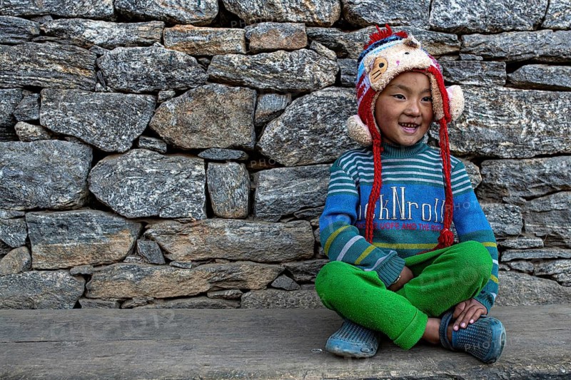 Happy smiling little Nepalese boy from the Sherpa ethnic group sitting in front of stone wall, Solu Khumbu Everest region, Himalayas, Nepal