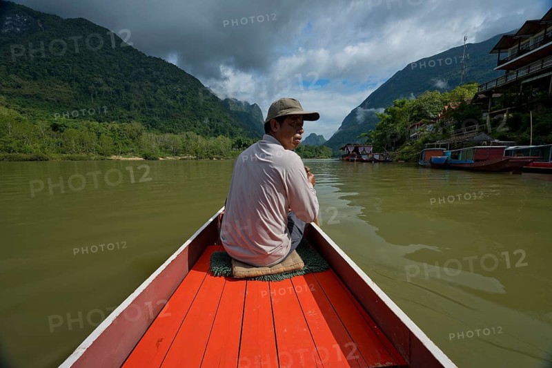 Laotian boat driver on a small boat in the mountainous landscape near the village of Muang Ngoi on the Nam Ou River, Phongsali province, Laos