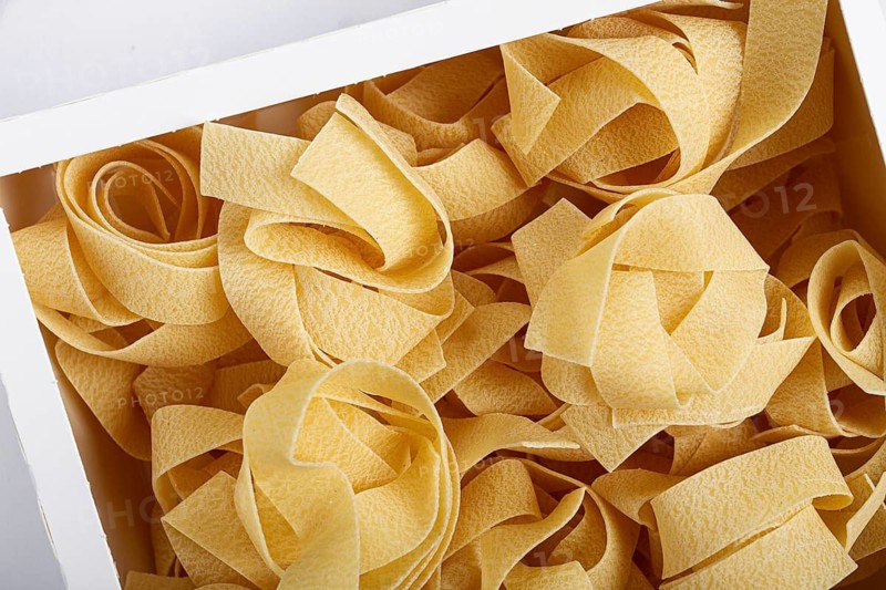 Raw pappardelle pasta, pasta nests, in a paper box, top view, no people