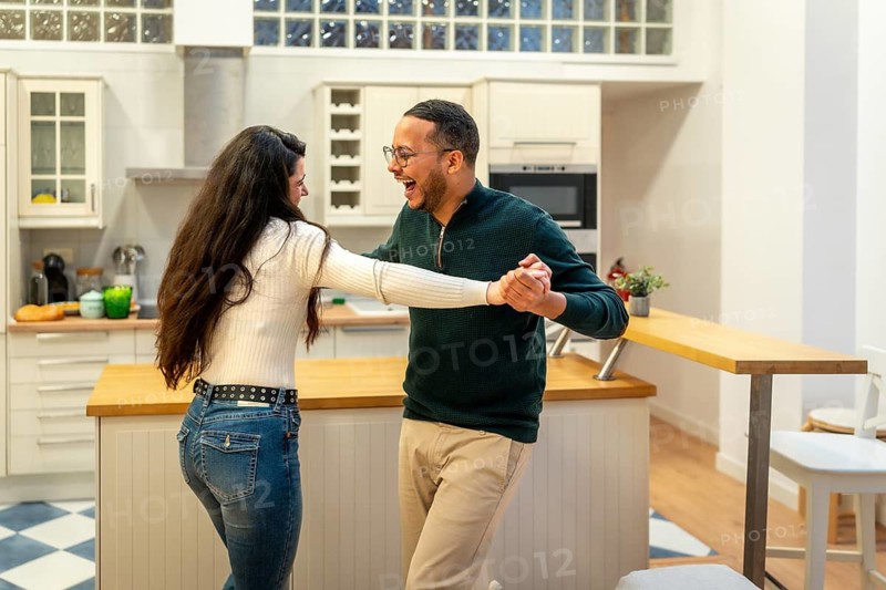 Happy diverse couple enjoying a fun moment together, dancing, laughing, and showing affection in a modern kitchen setting at home, celebrating love and togetherness
