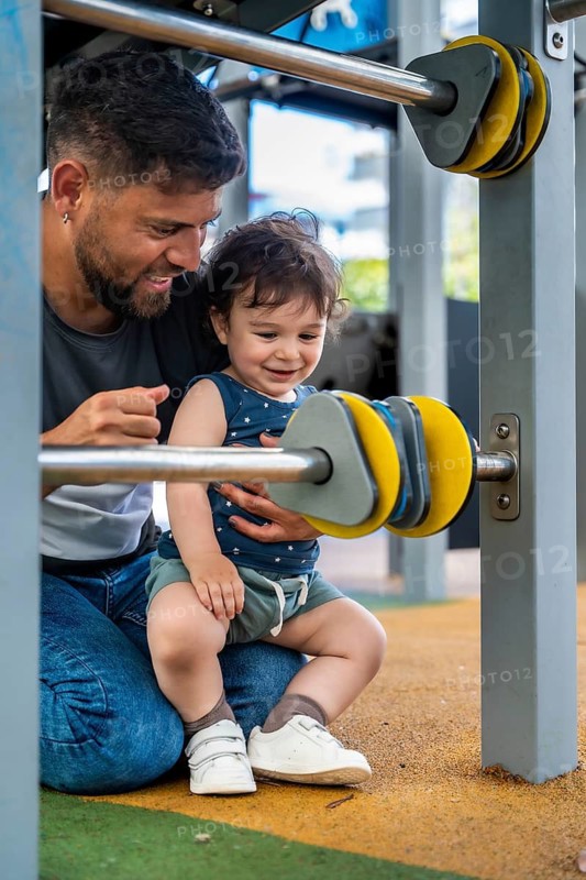 Happy father and toddler son enjoying time together, bonding and playing on a playground structure with colorful spinning elements, symbolizing family love and childhood joy