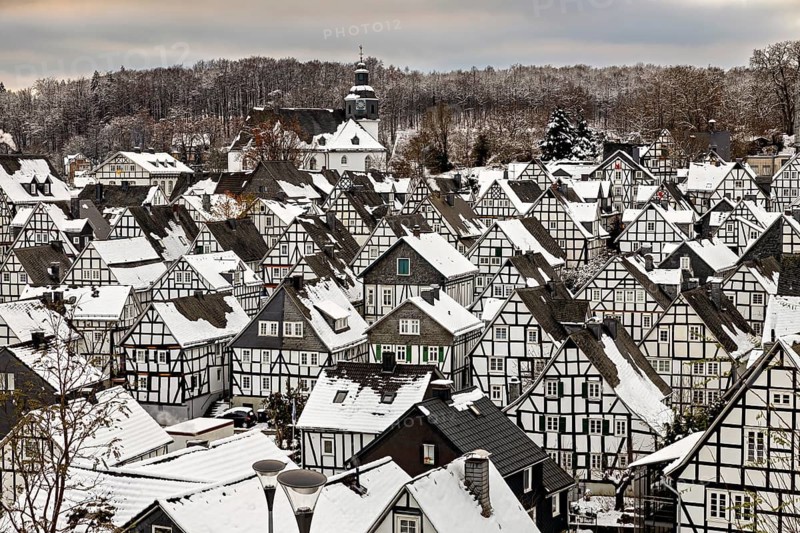 Close-up of snow-covered half-timbered houses and a church in the background, nestled in a wintery forest, The historic half-timbered houses from the Old Town in Freudenberg