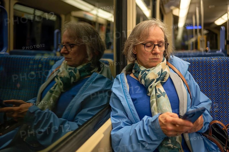 Interior view, elderly woman, glasses, sitting in S-Bahn, subway, train, typing on smartphone, cell phone, reflection, evening, night, night view, public transport, Stuttgart, Baden-Württemberg, Germany