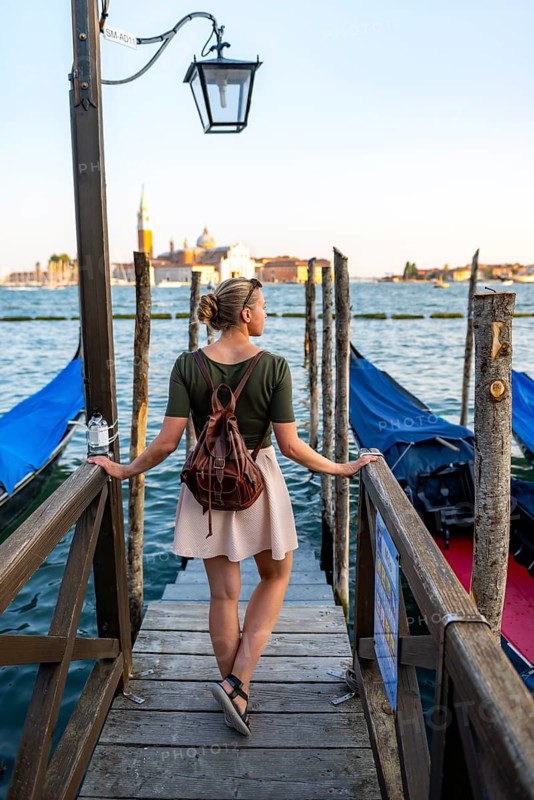 Young woman at a boat dock for Venetian gondolas in St. Mark's Square, tourist enjoying the evening, Venice, Veneto, Italy