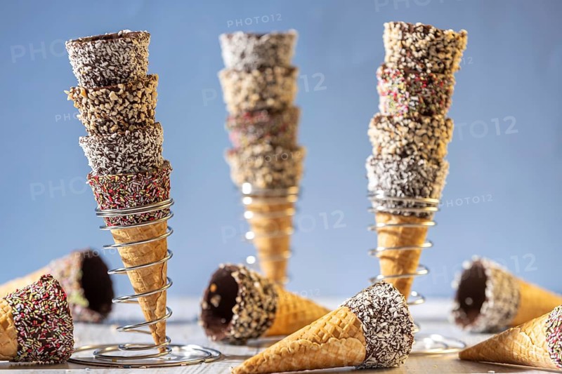 Ice cream cones stacked in metal stands, decorated with sprinkles and nuts