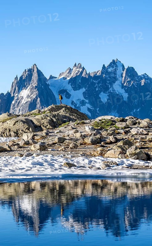 Young man in front of impressive mountain landscape in morning light, reflection in the Lac Blanc mountain lake, mountain summit, Aiguille Verte, Grandes Jorasses, Aiguille du Moine, Mont Blanc, Mont Blanc Massif, Chamonix-Mont-Blanc, Haute-Savoie, France