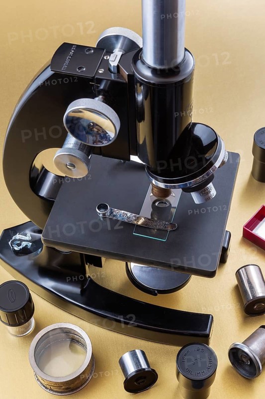Vintage black Bausch & Lomb research microscope with box of glass slides and objectives on light golden paper background, Studio Composition, Quebec, Canada