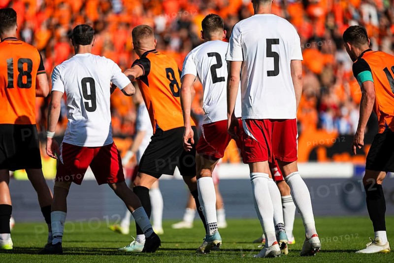 Professional soccer players in white and orange uniforms standing on the pitch during an intense football match stadium event with fans in Glogow, Poland