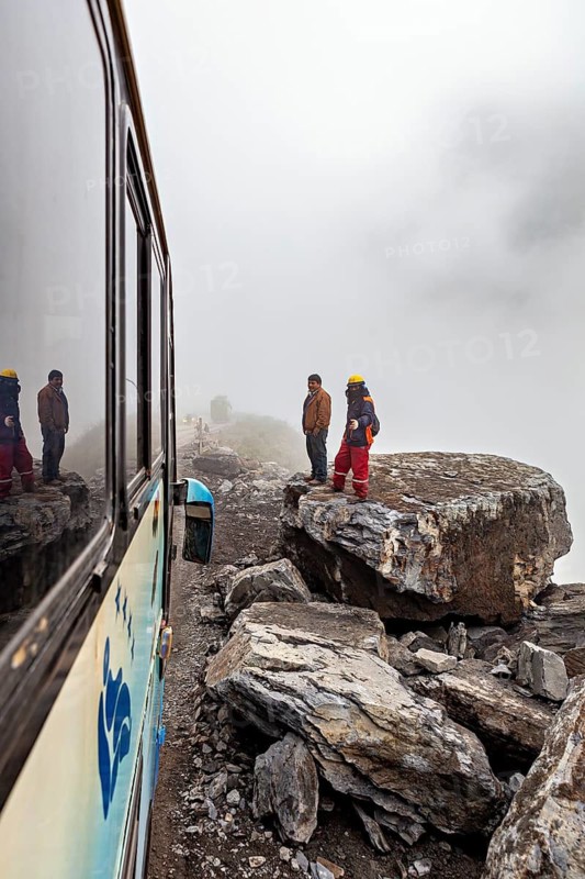 People in safety equipment on foggy cliffs next to a bus, adventurous atmosphere, rock slide on the pass road towards Rurrenabaque through the Andes on the road of death in Bolivia