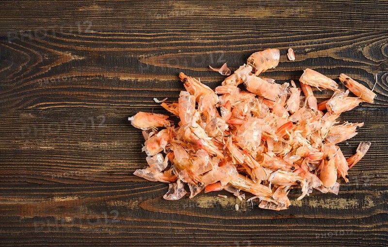 Shrimp shells on a wooden table. This shows a process of peeling and preparing shrimp for cooking. The shells are shown in a messy state, indicating a busy cooking environment