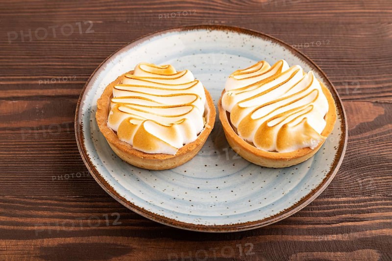 French lemon tart with meringue on brown wooden background, side view, close up