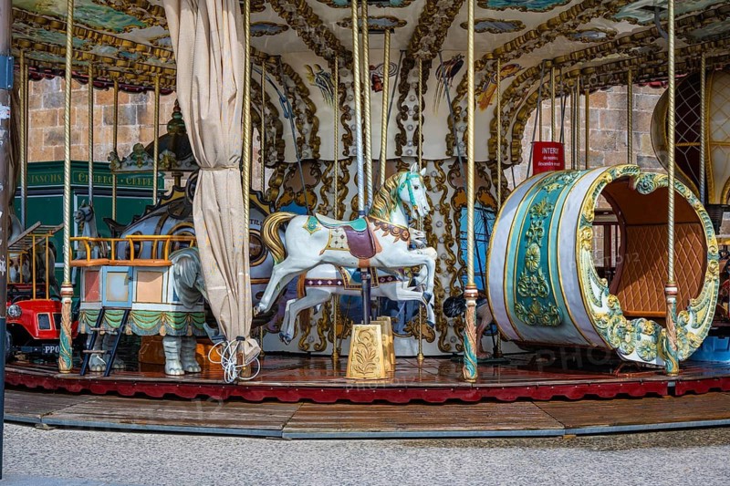 Nostalgic horse carousel at a fair with ornately decorated white carousel horses and a decorative carriage in historic French style, Saint Malo, Ille-et-Vilaine department, Brittany, France
