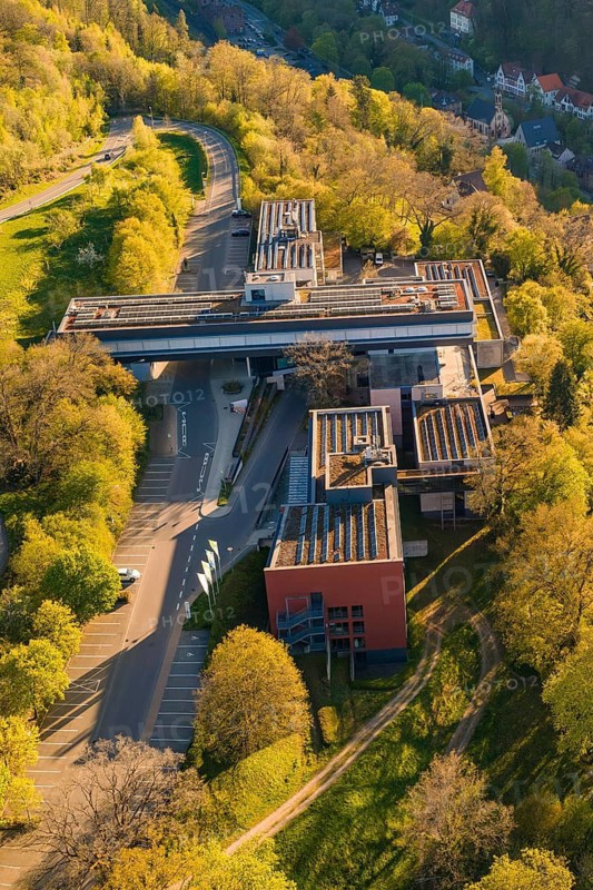 Aerial view of a modern building nestled in a green landscape with roads and trees under sunny spring weather, Calw District Office, Calw District, Germany
