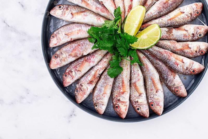Fresh mullet fish, laid out on a large platter, garnished with lime slices and cilantro, top view