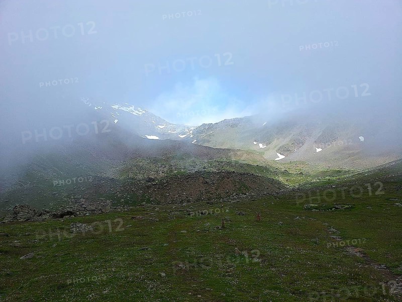 Cloudy mountain landscape with meadows and small snow-covered areas, E5, hiking in the Alps, crossing the Alps