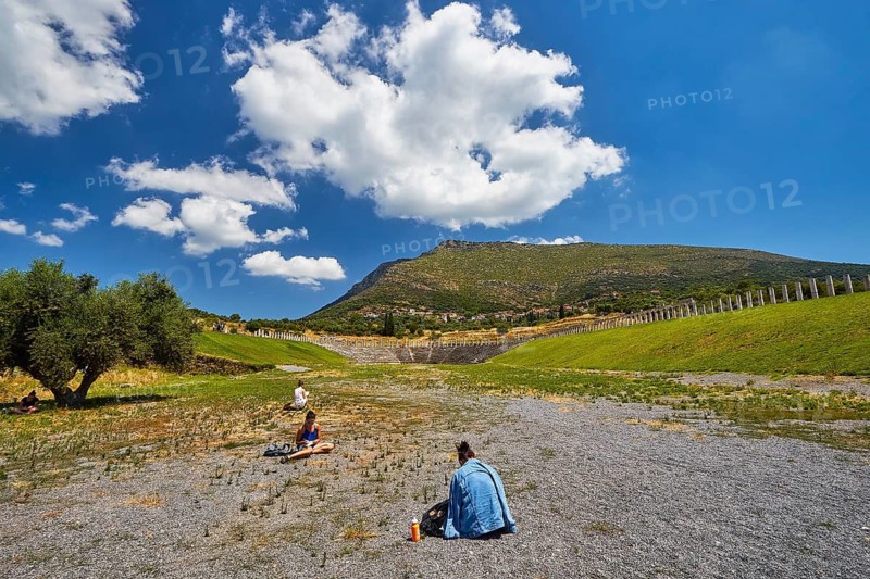 Two people sit in the courtyard of an ancient stadium with mountain background, Messene Stadium, Ancient Site, Archaeological Site, Messene, Messini, Messinia, Southwest of the Peloponnese, Odyssey, Odysseus, Ulysses, Film, Filming Location, Matt Damon, Peloponnese, Peninsula, Greece