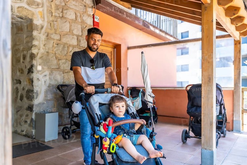 Father and young son spending quality time together, with dad pushing the child in a stroller on a building's covered walkway, representing family bonding and modern parenting