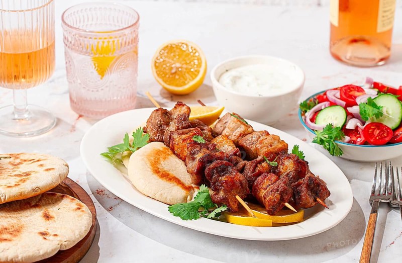 Souvlaki, a Greek dish, grilled meat shish kebab, on a plate with flatbreads, and lemon slices, grilled meat shish kebab, served with lavash, salad and drinks where there are no people