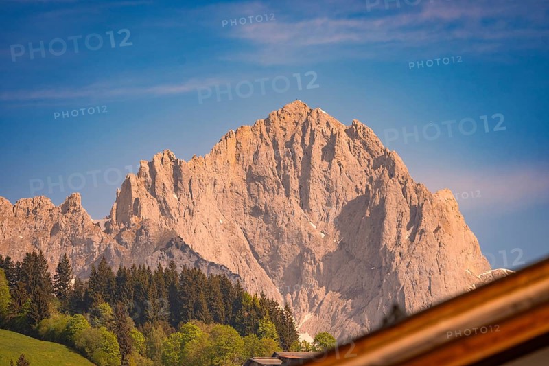 Rocky mountain peak against blue sky surrounded by trees and green hills, Hahnenkamm, Kitzbühel, Austria