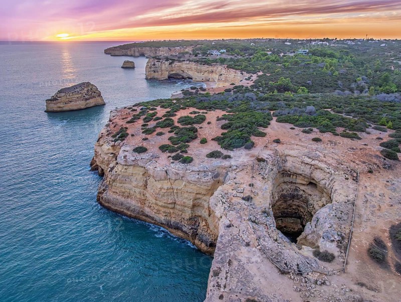 Drone sunset view of Arco de Albandeira at Praia de Albandeira in Algarve, Portugal, with limestone cliffs, Atlantic water, sea arch, and the natural arch centered above the cove