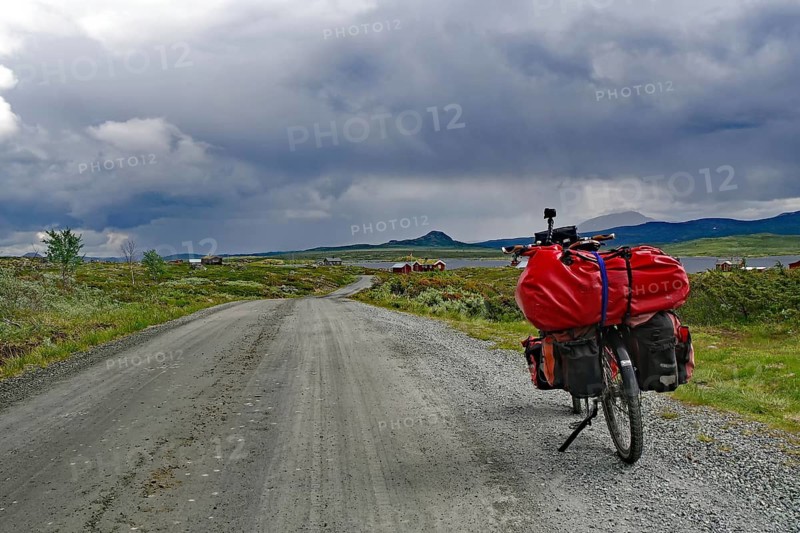 Bicycle with luggage on a dirt road under dramatic cloud formations, bicycle route, Jotunheimvegen, Mjolkevegen, Norway