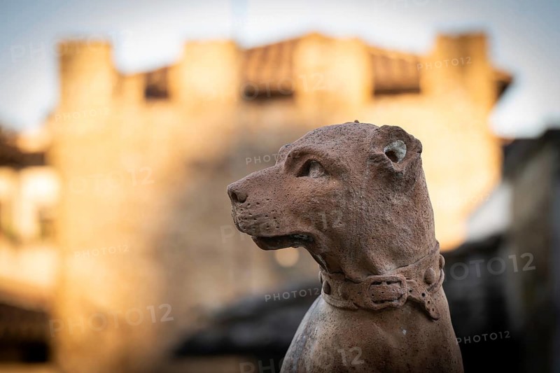 Terracotta statue of a dog with collar in front of blurred medieval building in the background, Bardini Garden or Giardino Bardini, Florence