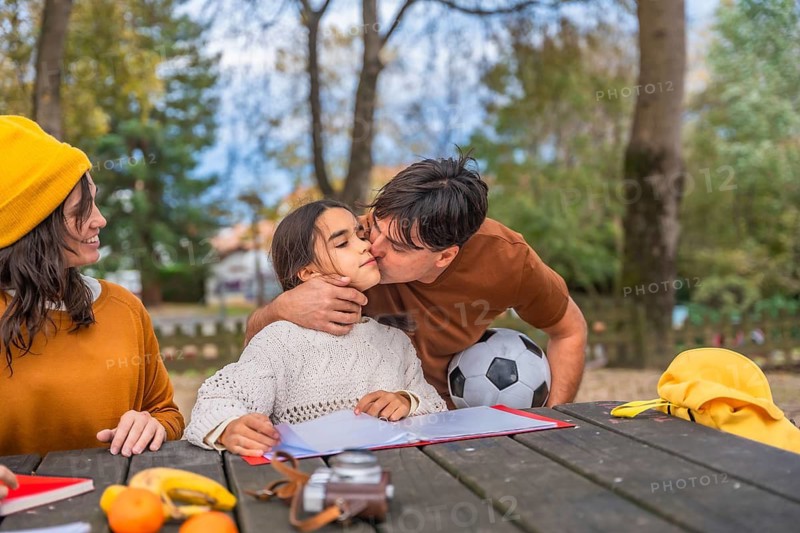 Family enjoying quality time together in a park setting, father affectionately kissing his daughter on the cheek while the mother smiles, sharing moments of love, bonding, and connection