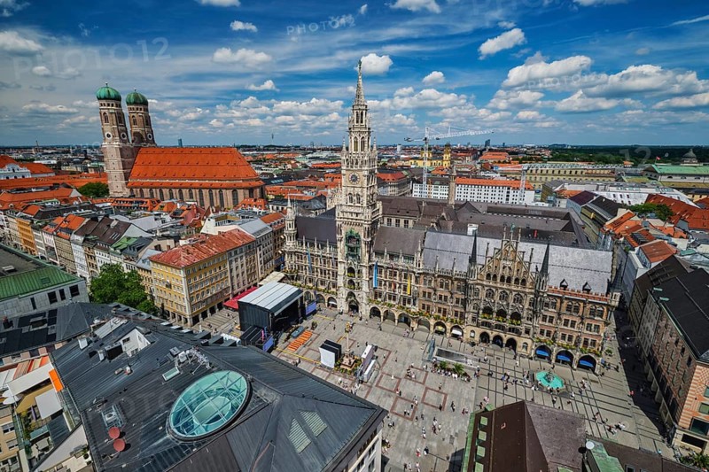 Wide high-angle view of the bustling Marienplatz square, the New Town Hall, and Frauenkirche under a blue sky in Munich, Bavaria, Germany
