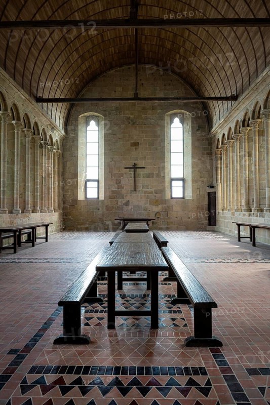 Interior view of the historic refectory, monks' dining room in the famous Benedictine Abbey of Mont Saint Michel. The 13th century Gothic hall features long wooden tables and wooden benches on a patterned tile floor under a vaulted wooden ceiling, Pontorson, Manche department, Normandy, France