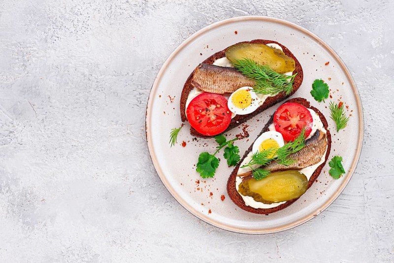 Sandwiches on rye bread, with sprats, quail eggs, fresh tomatoes and pickled cucumber, appetizer, breakfast, homemade